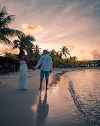 Rear view of couple walking on palm trees during sunset