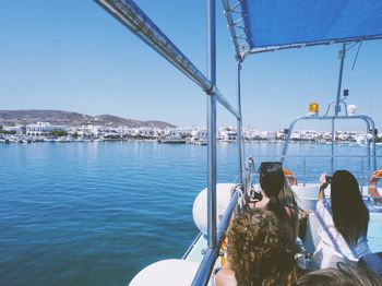 Rear view of people sitting on sea against clear sky