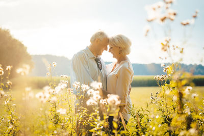 People on field by flowering plants against sky