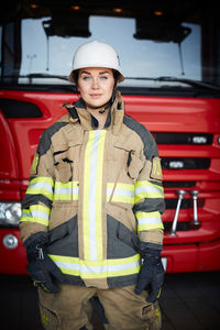 Portrait of confident firefighter standing in front of fire engine at fire station