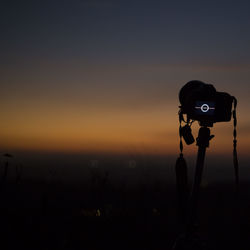 Silhouette of camera against sky during sunset