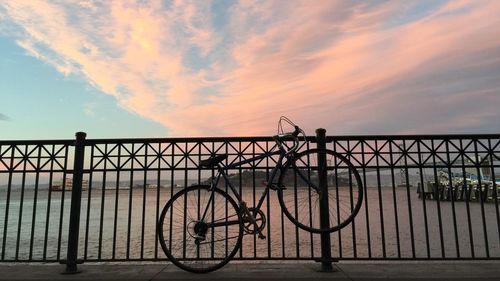Bicycle parked by railing at san francisco bay against sky during sunset