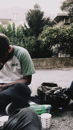 Rear view of man sitting by plants against trees