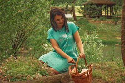 Full length of young woman holding wicker basket by plants