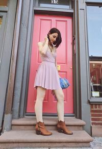 Young woman using phone while standing on window