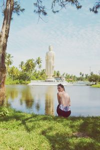 Man sitting by statue against lake