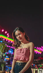 Portrait of woman standing against illuminated light at night