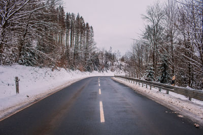 Road amidst bare trees against sky during winter