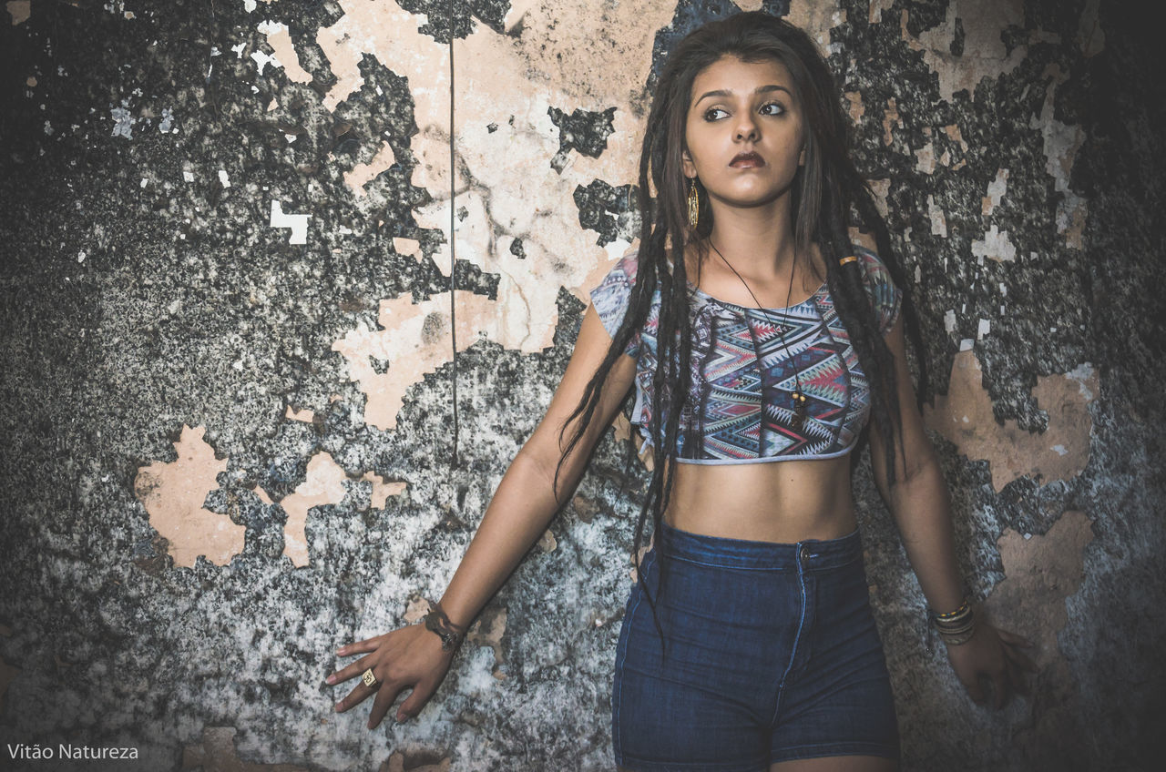 PORTRAIT OF YOUNG WOMAN STANDING ON WALL