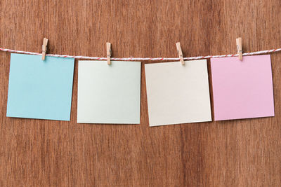 Close-up of notes hanging on clothesline against wooden wall
