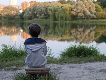 Little boy sitting ashore of lake. person sitting on a bench alone and watching sunset