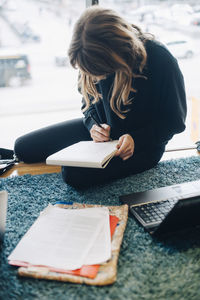 High angle view of businesswoman writing on notepad while sitting at office cafeteria