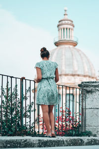 Rear view of woman standing by railing against sky