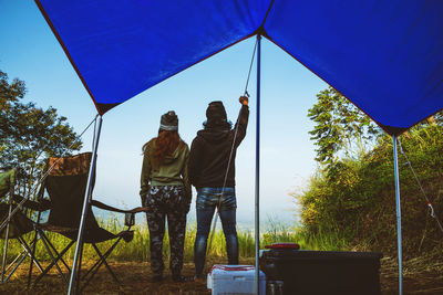 Rear view of couple standing at tent against blue sky