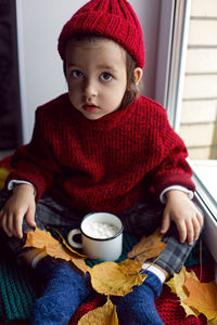 Boy a child in a red sweater and a knitted hat sits at the window on the windowsill