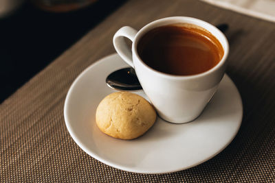 White cup of hot espresso coffee with a cookie on the table