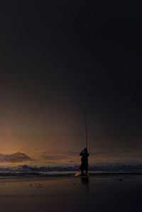 Silhouette man fishing at sea shore during sunset
