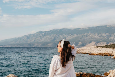 Rear view of young woman in white shirt standing on beach. sea, summer, view, lifestyle.