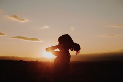 Mature woman standing on terrace against sky during sunset
