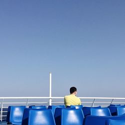 Rear view of man sitting on chair against clear blue sky