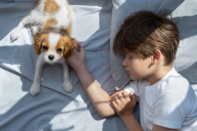 Boy with a dog in an embrace lies in bed . sleep with pets. cute puppy cavalier king charles spaniel