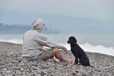 Man with dog sitting on pebbles