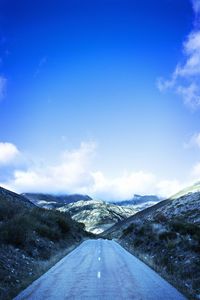 Road leading towards mountains against blue sky