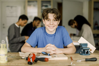 Portrait of smiling male teenage student with tools on table during carpentry class at high school