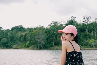 Woman looking away while standing by lake against sky