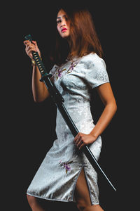 Portrait of young woman holding katana sword against black background