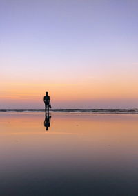 Silhouette man walking on beach against clear sky during sunset