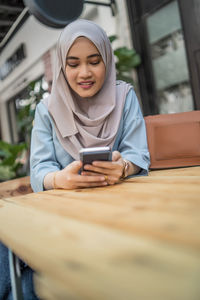 Low angle view of young woman using smart phone while sitting at sidewalk cafe