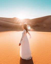 Woman standing on sand dune in desert against sky