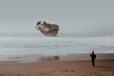 Rear view of woman walking at beach against clear sky