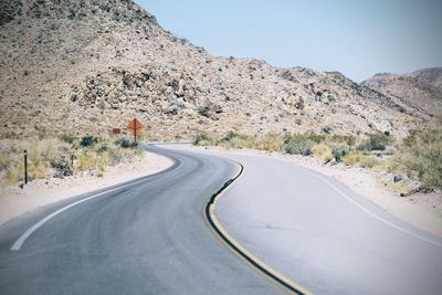 Empty road by mountains against clear sky