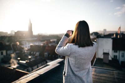 Rear view of man photographing cityscape against sky