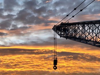 Low angle view of crane against cloudy sky during sunset