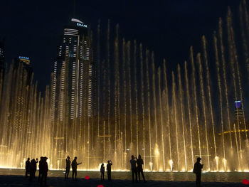 Silhouette people by illuminated building against sky at night