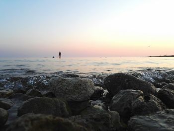 Mid distance view of man paddleboarding on sea against sky during sunset