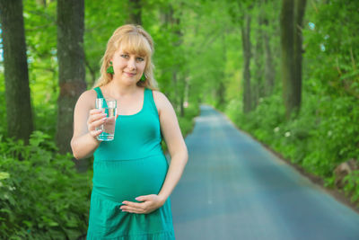 Portrait of pregnant woman with glass of water standing outdoors