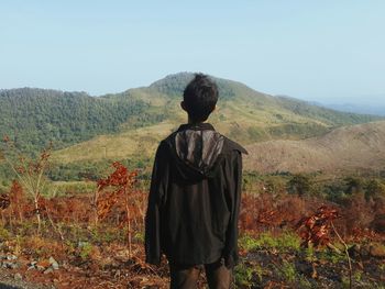 Rear view of man standing on field against mountain range