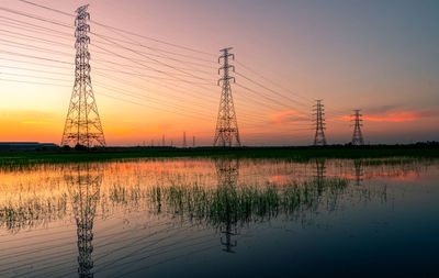 Reflection of electricity pylon on lake against romantic sky at sunset. high voltage electric pylon.