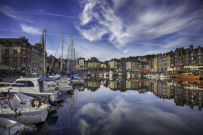 Sailboats moored at harbor against cloudy sky