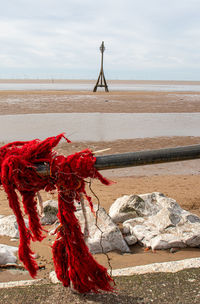 Red tied to rope on beach against sky
