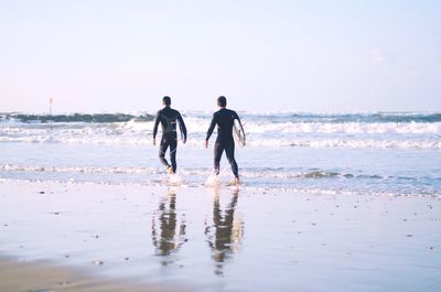 Rear view of surfers walking at beach against sky