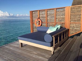 Empty chaise longue on wooden dock by sea against sky