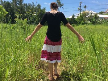 Rear view full length of woman standing amidst grassy field