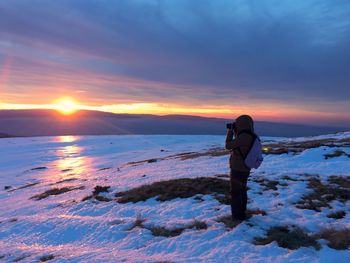 Rear view of woman photographing sea during sunset