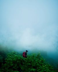 Rear view of man sitting on mountain against sky