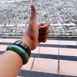 Cropped image of woman gesturing thumbs up against footpath